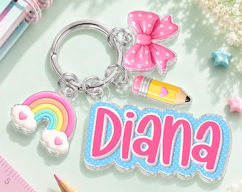 May include: A silver-toned metal keychain featuring a pink polka-dot bow charm, a yellow pencil charm with a heart, a rainbow charm with clouds, and a blue scalloped acrylic name tag with the name Diana written in bold pink letters.