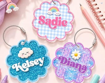 May include: Three scalloped acrylic keychains with metal wire loops. One features a blue gingham pattern with a rainbow and the name Sadie. Another has blue glitter with a white cloud and the name Kelsey. The third has purple glitter with a daisy and the name Diana.