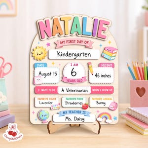K&ouml;nnte beinhalten: Ein h&ouml;lzernes Meilenstein-Schild f&uuml;r den ersten Kindergartentag mit dem Namen Natalie in bunten Buchstaben. Das Schild enth&auml;lt Felder f&uuml;r Datum, Alter, K&ouml;rpergr&ouml;&szlig;e von 117 cm, Berufswunsch, Lieblingsfarbe, Lieblingsessen, Tier und Lehrername.