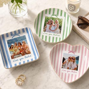 Puede incluir: Tres platos de cer&aacute;mica con bordes dorados, con rayas verticales en azul, verde y rosa. Cada plato muestra una fotograf&iacute;a personalizada de amigos y el texto escrito a mano "Love you Bestie" o "Love you Besties" con un peque&ntilde;o icono de lazo.