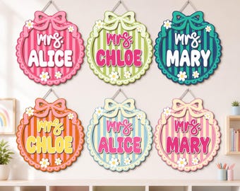 May include: Six circular wooden wall signs featuring vertical stripes, a scalloped border, and a decorative bow at the top. Each sign displays the text 'mrs.' in script and a name in block letters, accented with small white daisy flower cutouts.