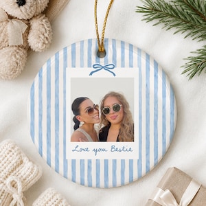 Puede incluir: Un adorno de cer&aacute;mica redondo con un patr&oacute;n de rayas verticales en azul claro y blanco. El centro muestra una foto cuadrada de dos personas con gafas de sol, enmarcada como una polaroid con un lazo azul y el texto Love you Bestie.