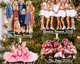 Puede incluir: Cuatro adornos acrílicos personalizados colgados en un árbol. Uno muestra una familia con un perro y el texto The Brown Family. Otro muestra un grupo de amigos con el texto Besties Forever 2026. Uno muestra tres niños con tutús rosas y el texto Beautiful Girly 2026. Uno muestra tres jugadores de fútbol americano con el texto The Boys 2026.