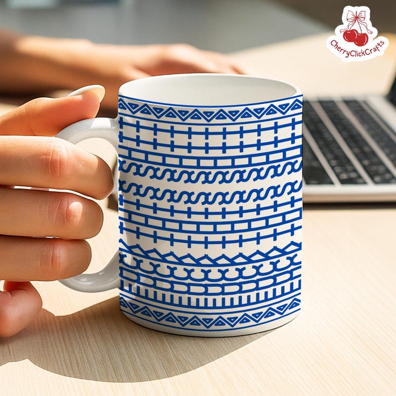 Puede incluir: Taza de cer&aacute;mica blanca con un patr&oacute;n geom&eacute;trico azul. El dise&ntilde;o presenta bandas horizontales de varias formas, incluyendo tri&aacute;ngulos, zigzags y figuras en forma de cruz. La taza tiene un asa blanca.