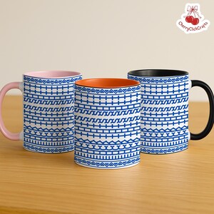 Puede incluir: Tres tazas de cer&aacute;mica con motivos geom&eacute;tricos azules sobre fondo blanco. Una tiene el interior y el asa rosas, otra el interior naranja y la tercera el interior y el asa negros. Las tazas est&aacute;n sobre una superficie de madera.