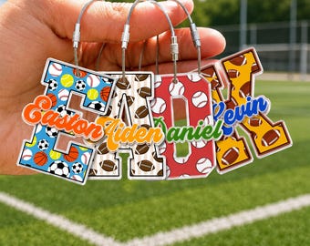 May include: Four acrylic letter-shaped keychains featuring sports-themed patterns. The letters spell Easton, Aiden, Daniel, and Kevin. Each keychain has a metal wire loop and displays colorful graphics of baseballs, footballs, and basketballs.