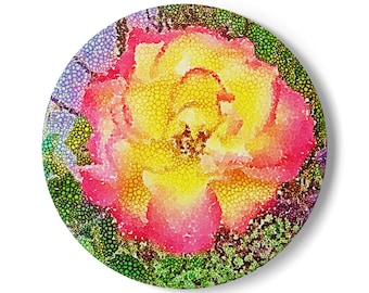 Puede incluir: Un posavasos redondo y decorativo con un diseño floral estilizado. La flor está representada en un estilo mosaico, con un degradado de tonos amarillos, rosas y rojos. El borde exterior presenta un patrón de puntos verdes y morados, creando un aspecto vibrante.