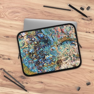 May include: A laptop sleeve with a colorful abstract design. The pattern features a mix of blue, gold, and orange hues, resembling a textured surface. The sleeve has a black border and a zipper closure.