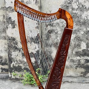 May include: A finely crafted wooden harp, stained a deep brown. The harp's frame is adorned with Celtic knot patterns, and the soundbox features detailed floral carvings. The strings are taut, ready for playing. The instrument is a beautiful example of craftsmanship.