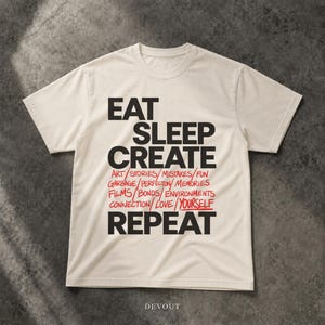 May include: A cream-colored short-sleeve t-shirt featuring the black text EAT SLEEP CREATE and REPEAT. Between these words is a list of red handwritten-style words: ART, STORIES, MISTAKES, FUN, GARBAGE, PERFECTON, MEMORIES, FILMS, BONDS, ENVIRONMENTS, CONNECTION, LOVE, YOURSELF.