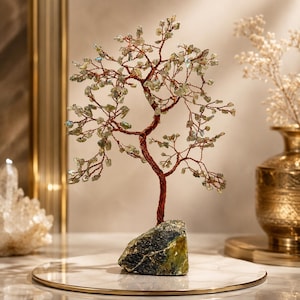Pode incluir: Uma escultura decorativa de árvore com um tronco e ramos de arame de cor cobre torcido, adornados com pequenas lascas de pedras preciosas translúcidas de cor verde pálido. A árvore está ancorada numa base de pedra natural texturizada.