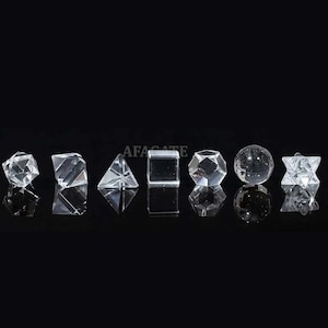 Könnte beinhalten: Eine Sammlung klarer geometrischer Kristallformen, darunter eine Kugel, ein Würfel, eine Pyramide und andere Polyeder. Die Formen werden auf einer reflektierenden schwarzen Oberfläche dargestellt. Das Wort "AFACATE" ist im Hintergrund sichtbar.