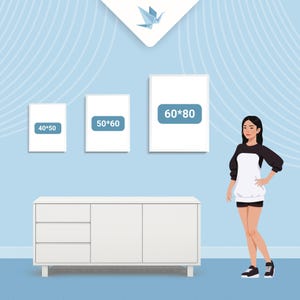 May include: Three framed art prints with dimensions labeled 40x50, 50x60, and 60x80 cm, displayed on a light blue wall. A white cabinet with three drawers and two doors is below the prints. A person is standing next to the cabinet.