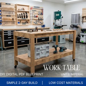 May include: A rectangular wooden work table with a lower shelf, mounted on four black casters. The table surface holds hand tools, while the lower shelf supports two stacked gray plastic storage cases, a cordless drill, and a sander.