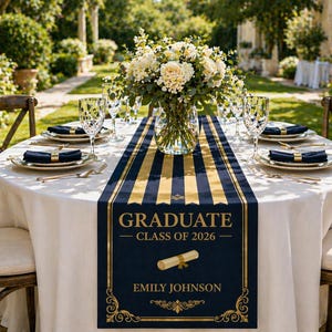 May include: A round table set for a graduation celebration, featuring a white tablecloth and wooden chairs. A navy blue and gold striped table runner displays the text "GRADUATE - CLASS OF 2026" and a name. The table is set with plates, napkins, and glassware, and a floral centerpiece.