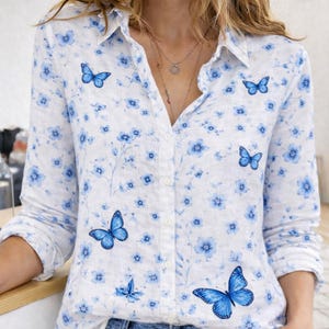 May include: White button-down shirt with a blue floral and butterfly pattern. The long-sleeved shirt features a classic collar and button closure. The butterflies are a vibrant blue, and the flowers are a lighter shade of blue.