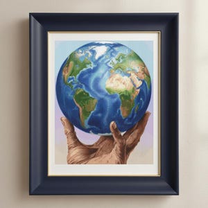 May include: A framed print featuring a detailed depiction of Earth held in a pair of hands. The artwork showcases the continents in shades of green and brown, surrounded by blue oceans. The frame is navy blue with a gold inner border.