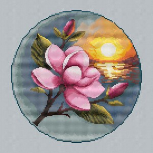 Può includere: Design a punto croce di un fiore di magnolia rosa con foglie e boccioli verdi, ambientato su un tramonto sull'acqua. L'opera è incorniciata in un cerchio verde acqua, creando una scena serena e naturale.