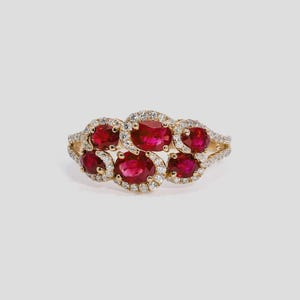May include: A gold ring featuring seven oval-cut rubies surrounded by small diamonds. The rubies are a vibrant red, and the diamonds sparkle against the gold setting. The ring has a delicate, yet eye-catching design.