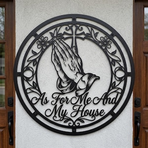 Könnte beinhalten: Schwarze Metall-Wandkunst mit betenden Händen in einem kreisförmigen Rahmen. Das Design umfasst ein Kreuz, florale Akzente und den Text "As For Me And My House". Ein dekoratives Stück für die Haus- oder Außendekoration.