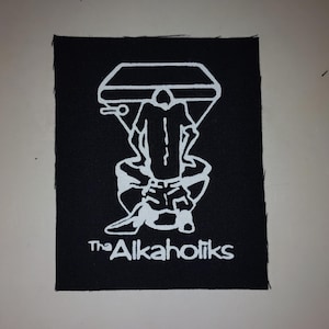 May include: Black square patch featuring a white graphic of a person on a toilet, holding a microphone. The text "The Alkaholiks" is below the graphic in white.