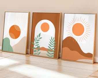 Könnte beinhalten: Drei gerahmte Kunstdrucke mit abstrakten Landschaftsdesigns. Jeder Druck zeigt eine warme Farbpalette mit orangefarbenen Sonnen, erdfarbenen Bergen und grünem Laub. Die Rahmen sind hellholzfarben.