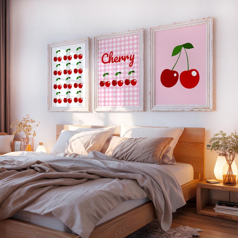 May include: Three framed cherry-themed wall art pieces. One features rows of cherries, another has the word "Cherry" with cherries below, and the last shows two cherries. The frames are white, and the backgrounds are white, pink, and a pink gingham pattern.