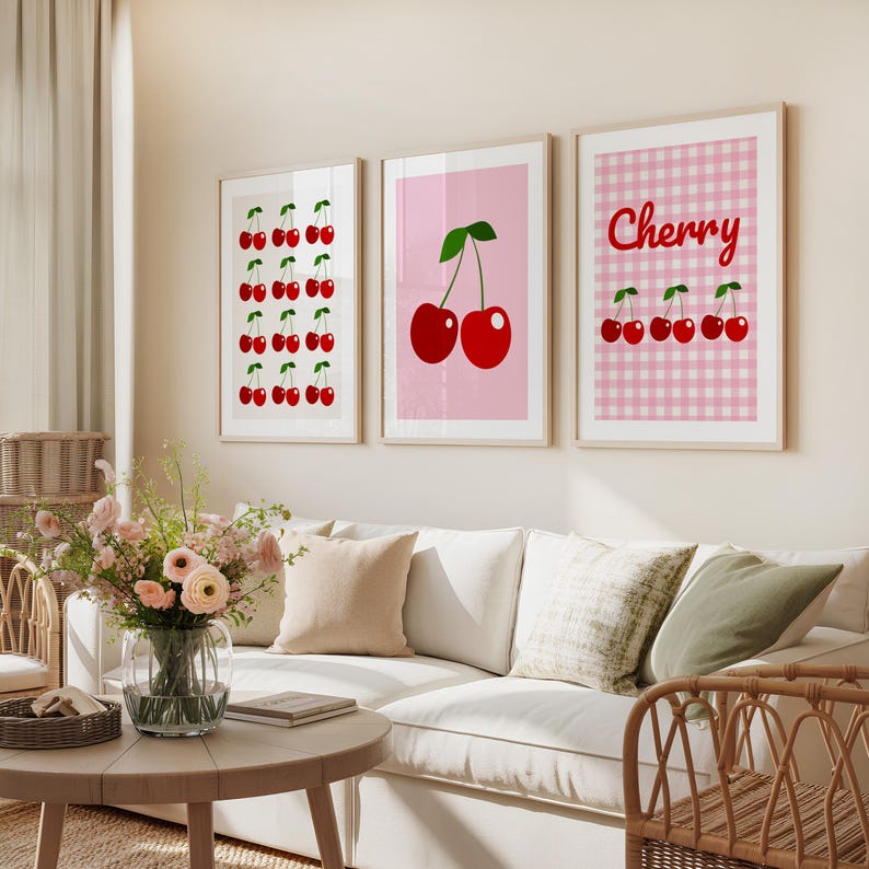 May include: Three framed art prints featuring cherry designs. One print displays rows of red cherries with green stems on a white background. Another shows two cherries on a pink background. The third print has a pink gingham pattern with the word "Cherry" and cherries.