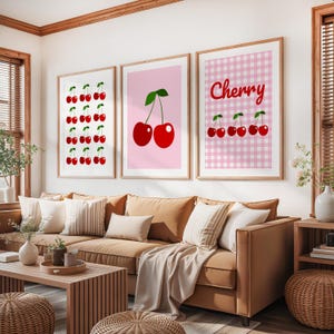 May include: Three framed art prints featuring cherry designs. One print displays rows of cherries, another shows two cherries, and the third has a gingham background with the word "Cherry" and cherries.