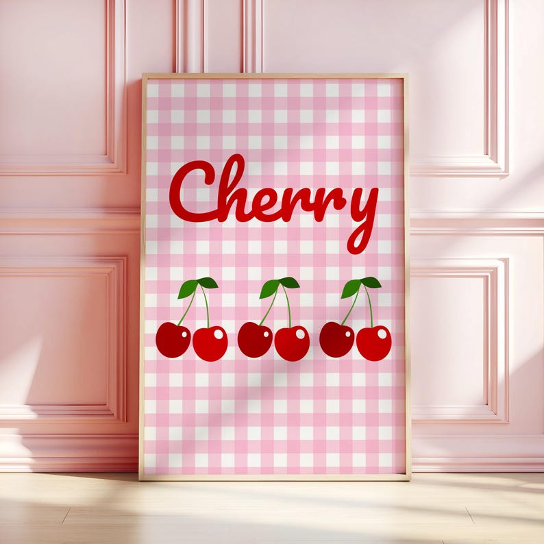 May include: A framed print featuring the word "Cherry" in red script above a row of red cherries with green stems. The background is a pink and white gingham pattern, creating a playful and cheerful aesthetic.