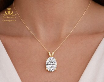 May include: A gold necklace with an oval-cut diamond pendant. The diamond is set in a gold bezel and hangs from a delicate gold chain. The necklace is displayed on a person's neck. The brand name "Balkrushna Gems & Jewels" is visible.