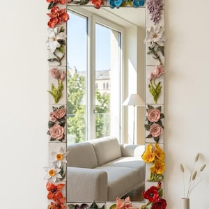 Könnte beinhalten: Ein rechteckiger Wandspiegel mit einem Rahmen, der mit dreidimensionalen Keramikblumen in verschiedenen Farben wie Rot, Blau, Rosa, Gelb, Weiß und Violett verziert ist. Die Blumenelemente sind auf einzelnen weißen Fliesen angebracht.