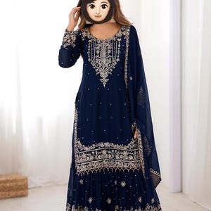 Può includere: Un abito formale blu navy ricamato con una sciarpa abbinata. L'abito presenta intricati ricami dorati intorno allo scollo, alle maniche e all'orlo. L'abito a maniche lunghe ha una gonna svasata ed è adatto alle occasioni speciali.