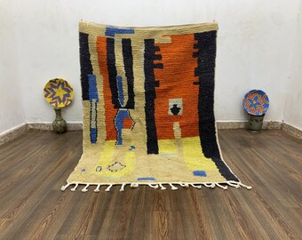 Puede incluir: Una alfombra rectangular tejida a mano con un fondo beige y un diseño geométrico colorido. El diseño incluye rayas verticales en negro, naranja y azul, con acentos amarillos y blancos. La alfombra tiene una franja a lo largo del borde inferior.