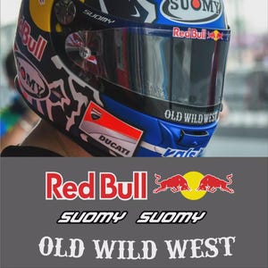 以下が含まれることがあります： バイザー付きのオートバイ用ヘルメット。Red BullとSuomyのロゴ、そして「OLD WILD WEST」の文字が特徴です。ヘルメットは青、白、黒、黄色の配色で、Ducatiのブランドが入っています。アンドレア・ドヴィツィオーゾのヘルメットの画像です。