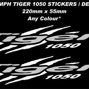 Puede incluir: Dos pegatinas o calcomanías blancas de Triumph Tiger 1050 con un diseño gráfico de marcas de garras. El texto dice TRIUMPH TIGER 1050 STICKERS | DECALS, 220mm x 55mm, y Any Colour*. El diseño se presenta sobre un fondo negro sólido.