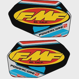 Puede incluir: Dos pegatinas hexagonales negras con un diseño amarillo, rojo y azul. Las pegatinas presentan el texto "FMF SO. CALIF." y "POWERCORE 2". El diseño incluye una bandera estadounidense estilizada.