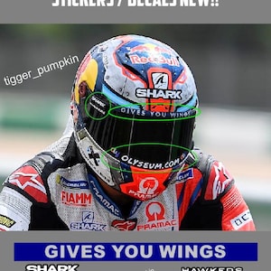 Könnte beinhalten: Ein Set aus Visieraufklebern und Abziehbildern für einen Jorge Martin Helm mit dem Text GIVES YOU WINGS, SHARK, HAWKERS und OLYSEUM.COM. Die Aufkleber werden zusammen mit einem Bild eines Motorradhelms mit diesen spezifischen Markenlogos gezeigt.