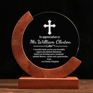 May include: A commemorative award featuring a glass disc with a cross and text, set in a wooden frame and base. The text reads "In appreciation to Mr. William Clinton" and a thank you message. The wood has a warm, brown tone.