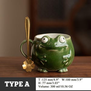 May include: A green ceramic frog-shaped mug with a matching gold-colored spoon. The mug is 4.9 inches wide, 3.9 inches in diameter, and 3.03 inches high. The mug holds 10.56 ounces. The text "TYPE A" is at the bottom.