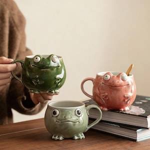 May include: A white ceramic mug with a black handle and the text "But First, Coffee" in a black, bold font. The mug is sitting on a wooden surface. The mug is approximately 4 inches tall.