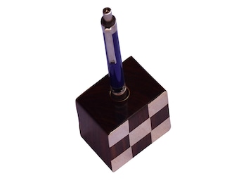May include: A pen holder with a blue pen. The pen holder is a dark brown cube with a checkerboard pattern on the front and side. The pen is blue with silver accents.