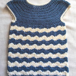 Puede incluir: Top de crochet hecho a mano con diseño sin mangas. El top presenta bandas alternas de azul marino y blanco roto, creando un patrón de chevrón. El escote y las sisas están ribeteados con crochet blanco roto.
