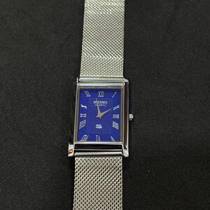 May include: A rectangular Seiko Quartz watch with a blue face and silver mesh band. The watch face features Roman numerals and the Seiko logo. The watch is displayed against a dark background.