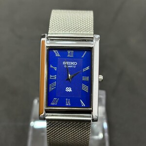 May include: A rectangular Seiko Quartz watch with a silver mesh band. The watch face is a vibrant blue with silver Roman numerals and hands. The watch case is silver, and the watch is displayed on a clear stand.