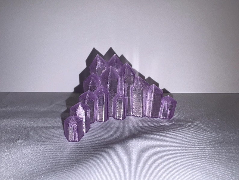 K&ouml;nnte beinhalten: Eine Ansammlung von lila Kristallformationen, m&ouml;glicherweise Amethyst, in einem Halbkreis angeordnet. Die Kristalle haben ein facettiertes Design und sind vor einem neutralen Hintergrund platziert, wodurch ein Spiel von Licht und Schatten entsteht.