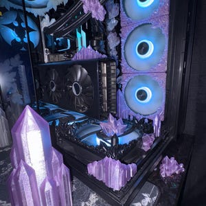Puede incluir: Un ordenador personalizado con una carcasa negra, adornado con detalles en forma de cristal púrpura y ventiladores azules brillantes. Los componentes incluyen una tarjeta gráfica y un sistema de refrigeración líquida.