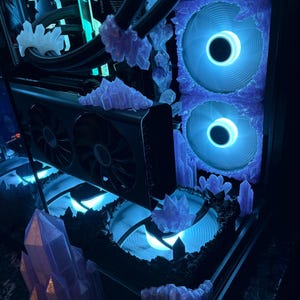 K&ouml;nnte beinhalten: Ein individuell angefertigtes Computergeh&auml;use mit einer einzigartigen &Auml;sthetik. Das Innere ist mit blauen Lichtern beleuchtet und mit kristallartigen Strukturen verziert. Die L&uuml;fter und Komponenten sind sichtbar, was ein futuristisches und k&uuml;nstlerisches Design ergibt.