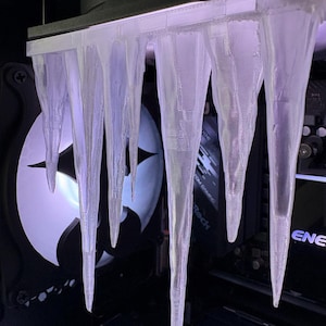 May include: A custom computer case modification featuring a series of clear, icicle-shaped ornaments hanging from a black structure. The icicles are translucent, with visible internal structures, and are illuminated by a soft, purple light.