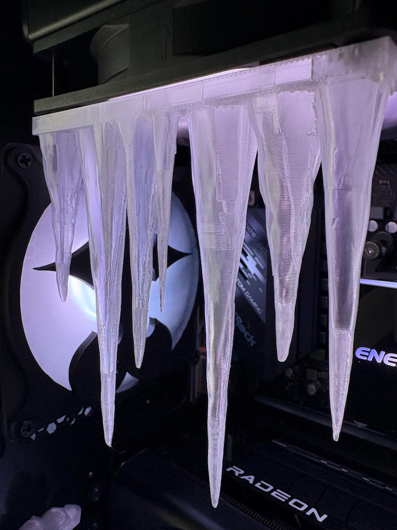 May include: A custom computer case modification featuring a series of clear, icicle-shaped ornaments hanging from a black structure. The icicles are translucent, with visible internal structures, and are illuminated by a soft, purple light.